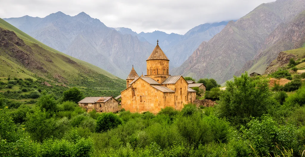 Monastère arménien ancien niché dans une vallée verdoyante avec montagnes du Caucase en arrière-plan